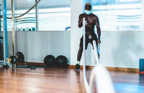 Young black man doing workout session with battle rope while wearing face mas Stock Photos