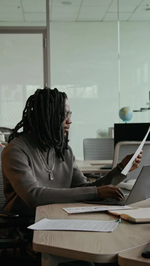 Young Black Man with Dreadlocks Working with Laptop and Papers in Office Stock Footage 333392069