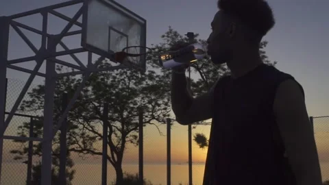Young black man drinking water while playing basketball on playground on sunrise 動画素材 160476736