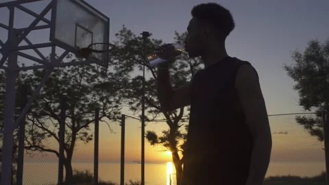 Young black man drinking water while playing basketball on playground on sunrise 動画素材 160476762