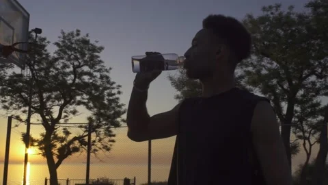 Young black man drinking water while playing basketball on playground on sunrise 動画素材 160476785