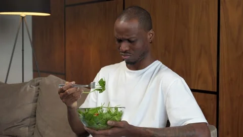 Young black man forcing himself to eat salad, dissatisfaction, diet for weight Stock Footage 168744411