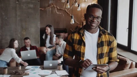 Young black man holding tablet in modern loft office with colleagues working on Stock Footage 132746522