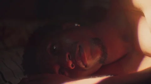 Young Black Man Lying Awake in Bed Illuminated by Morning Sunlight Stock Footage 316543155