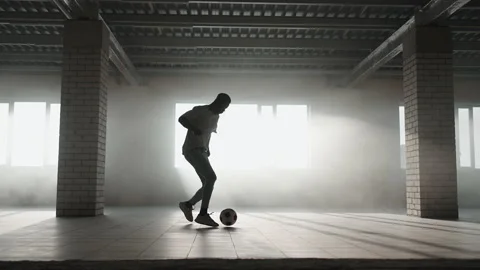 A young black man practices football dribbling in an underground parking lot in Stock Footage 154792353