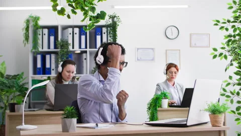 Young black man taking off headset and celebrating successful deal while working 스톡 동영상 306143576