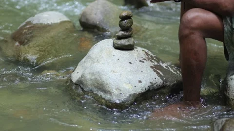 A Young Black Man Trying to Make a Stack of Rocks Stock Footage 207656475
