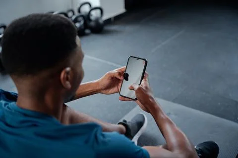 Young black man typing on mobile phone while taking a break at the gym Stock Photos