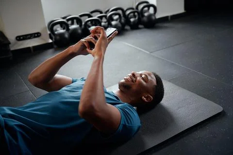 Young black man typing on mobile phone while resting at the gym Stock Photos