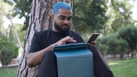 Young black man working remotely in a park with a tablet 스톡 동영상 287491424