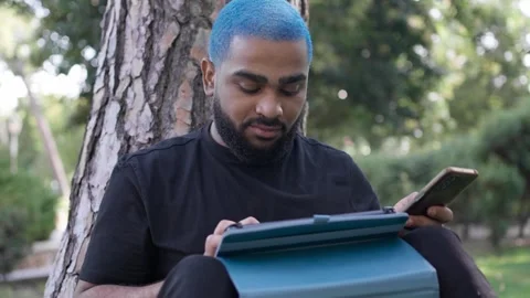 Young black man working remotely in a park with a tablet 스톡 동영상 287491468