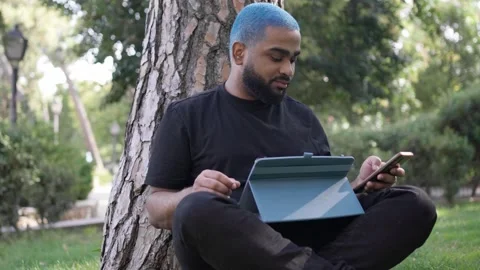 Young black man working remotely in a park with a tablet 스톡 동영상 287491501