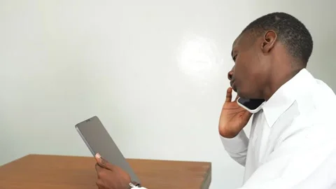 Young black man working on a tablet in an office at a table receives a call 스톡 동영상 278477560