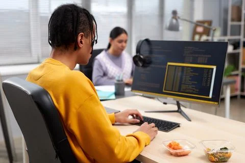 Young black man writing code while working at desk in office Stock Photos