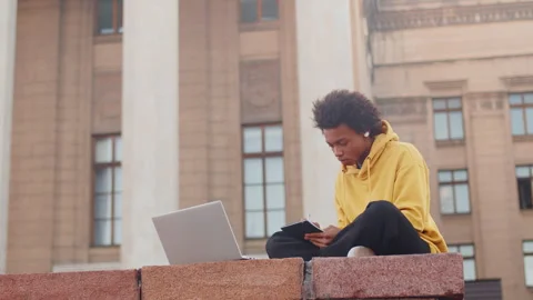 Young black programmer in casual clothes sitting with a laptop outdoors near the Stock Footage 280142135