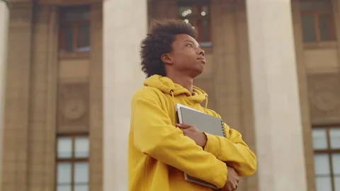 Young black programmer with a laptop and a copybook dreamily gazing into the Stock Footage 262069380