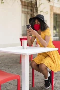 Young black woman with curly hair, with red mask, yellow dress and black hat, Stock Photos