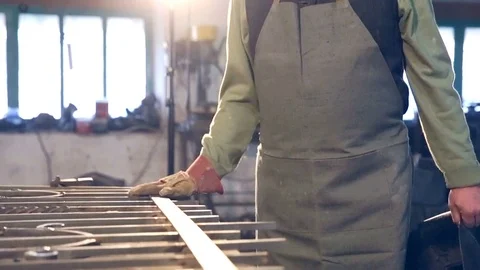 A young blacksmith close-up hand in gloves touches metal products Stock Footage 77005435
