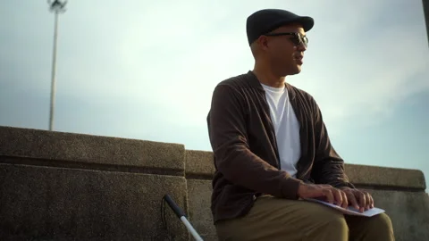The young blind man reading braille while sitting on the bench in the city park. Stock Footage 276485378