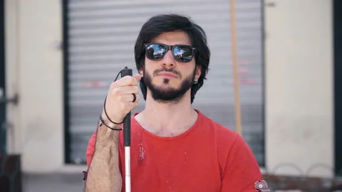 Young blind man sitting on a bench holding his white cane Video stock 131973232