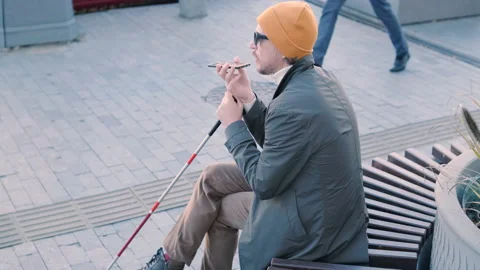 Young blind man with smartphone sitting on bench in park in city, calling Stock Footage 221397693