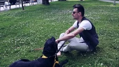 Young blind man with white cane and guide dog sitting in park in