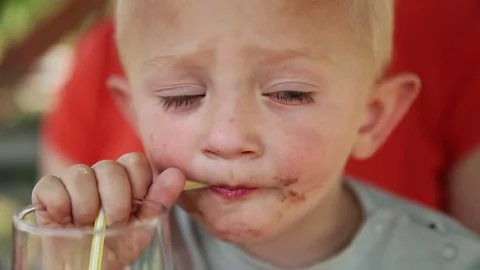 Young blond boy with dirty face drinking lemonade from a straw looking around Stock-Footage 73776610