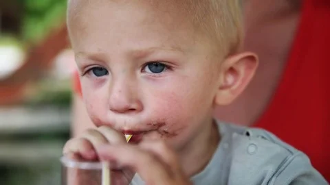 Young blond boy with dirty face drinking lemonade from a straw looking around 库存影片 73776744