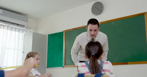 Young blond boy raises hand from wooden desk to answer teacher question while 库存影片 335458688