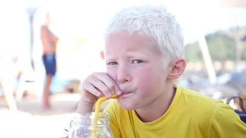 A young blond boy sitting in a cafe on the beach and drinking juice from a straw Stock Footage 88800653