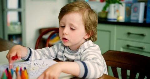 Young Blond Boy Sitting At Kitchen Table Using Crayons Stock Footage 100042853