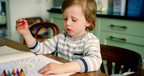 Young Blond Boy Sitting At Kitchen Table Using Crayons Stock Footage 100042871