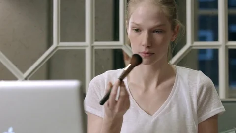 Young blond is doing her own makeup while watching tutorial on her  laptop Video stock 74669928