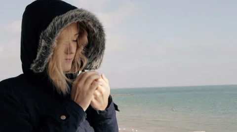 Young blond girl in down jacket basking in the sun on the beach and smiling Stock Footage 61963290