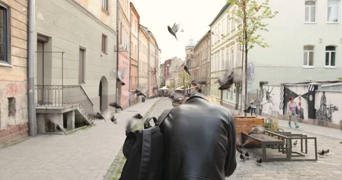 Young blond guy in a black jacket with a backpack scared when the doves began to Video stock 126576017