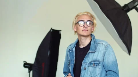 A young blond guy in a black t-shirt and denim jacket poses in the Studio for a Stock Footage 135863587