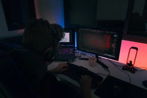 Young blond guy playing video games on a computer with headphones and using a Stock Photos