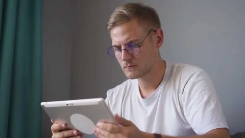 Young blond guy works on a tablet at home Stock Footage 221261081