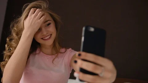 Young blond lady taking selfies ,sitting on the bed in a pink pajama Stock Footage 73820194
