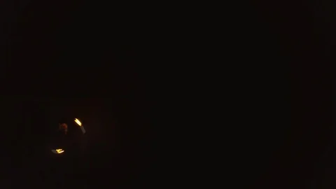 Young blond male does fire dance with two torches, spins burning torches. Drone Stock Footage 105220831
