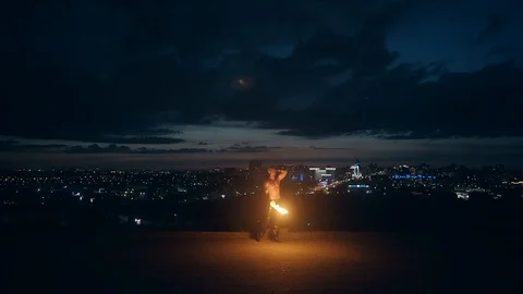 Young blond male does tricks with fire, breaths fire at night with city skyline Stock-Footage 105213746