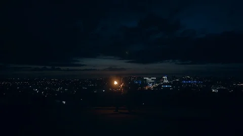 Young blond male does tricks with fire, breaths fire at night with city skyline Stock Footage 105213775