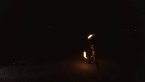 Young blond male does tricks with fire, spins two burning torches at night on Stock Footage 105220540
