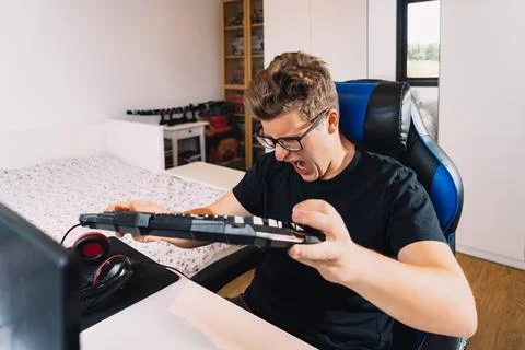Young blond man banging on the keyboard in anger at losing a video game on his Stock Photos