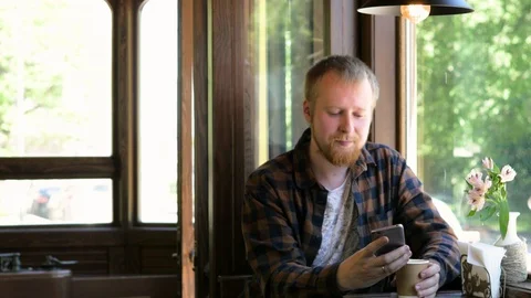 Young blond man drinks coffee from a disposable cup in a cafe. A man holds a Stock-Footage 118079092