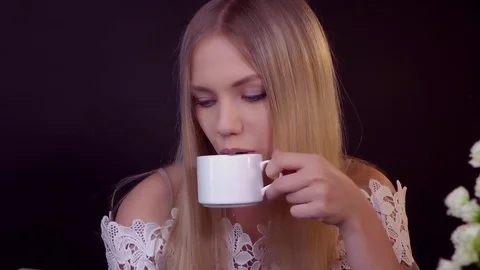 Young blonde on a black background. She drinks her coffee and reads a text Stock Footage 79244855