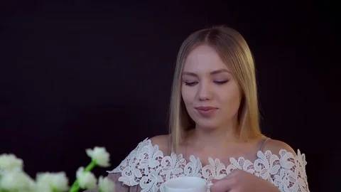 Young blonde on a black background. She drinks her coffee and looks dreamily Stock Footage 79245489