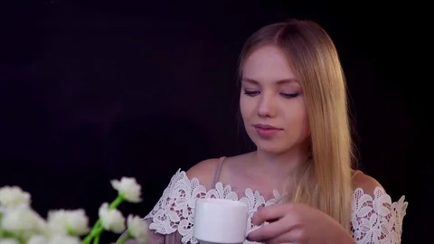 Young blonde on a black background. She drinks her coffee and looks dreamily. Stock Footage 79249110