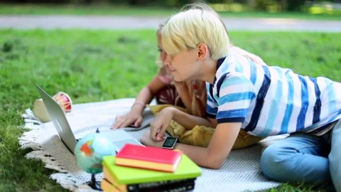 Young blonde boy with smartwatch using laptop in sunny park outdoor. Learning on 스톡 동영상 137327099