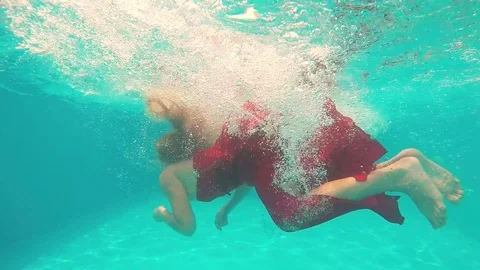 Young blonde girl in long red dress jumps into the swimming pool Stock Footage